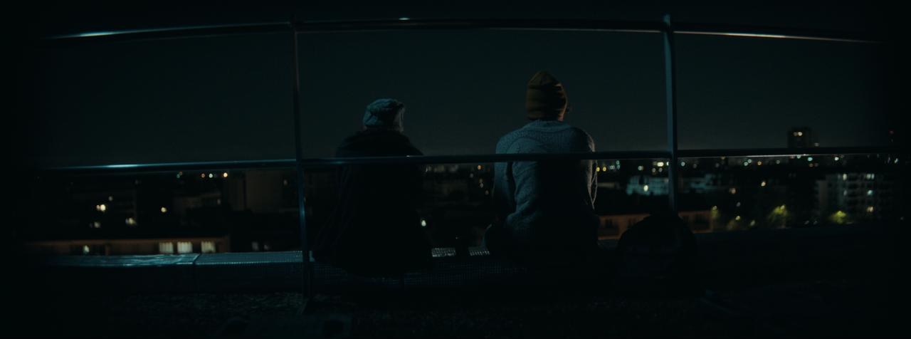 Deux silhouettes assises sur le toit du lycée, face à la ville la nuit